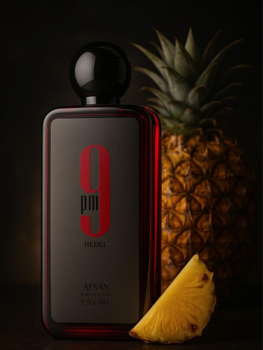 Botella de eau de parfum 9pm Rebel de AFNAN con piña fresca al fondo y una rodaja de piña